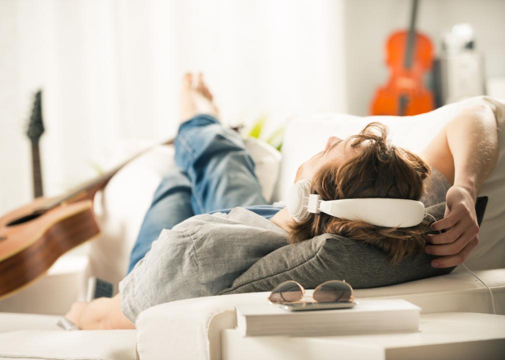 A young man laying on the couch listening to music