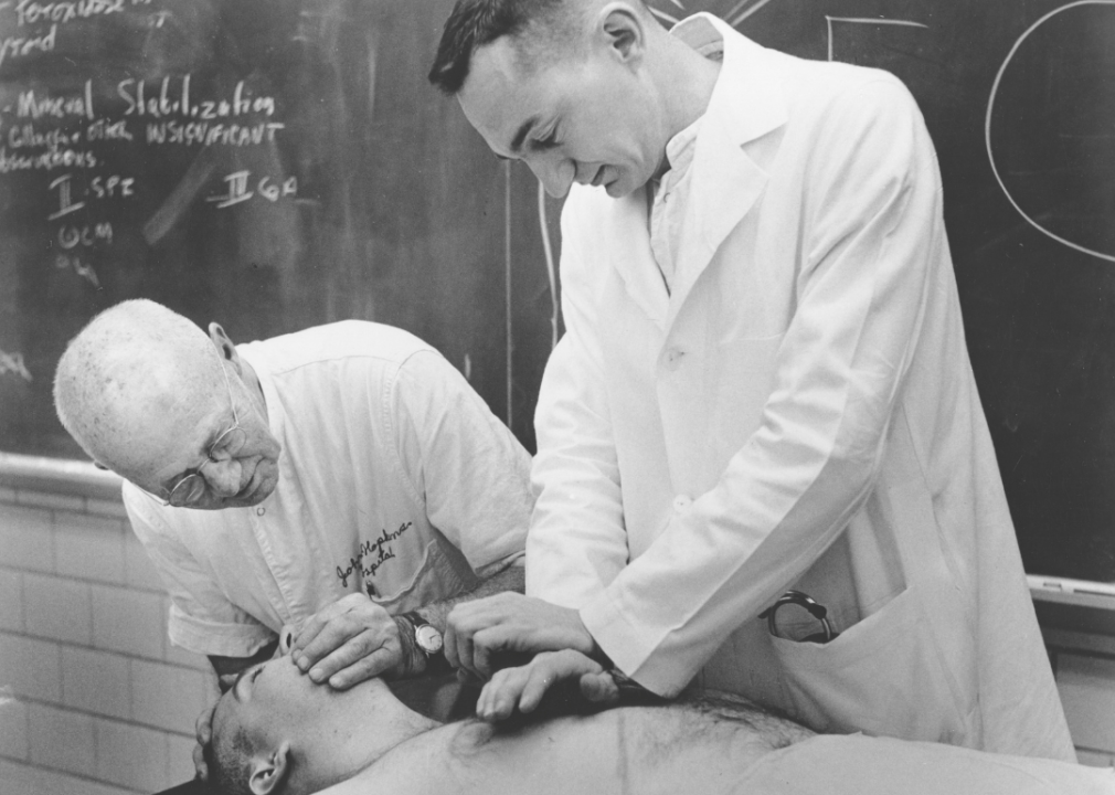 Dr. William Kouwenhoven bending over man on table while demonstrating techniques of CPR